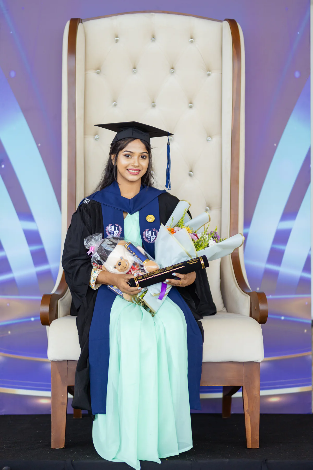 A CCA graduate in academic dress holding flowers and her graduation scroll